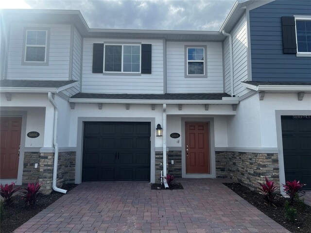 entrance to property with a garage, stone siding, decorative driveway, and roof with shingles