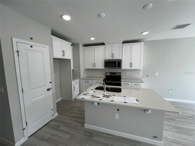 kitchen with appliances with stainless steel finishes, an island with sink, visible vents, and white cabinets