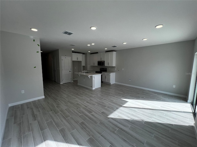 kitchen featuring a kitchen island, visible vents, white cabinets, open floor plan, and stainless steel microwave