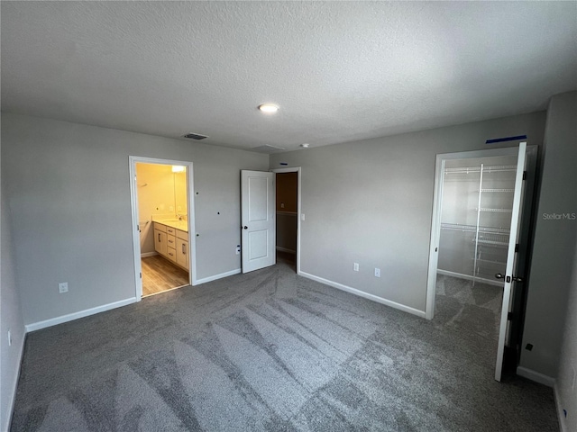 unfurnished bedroom featuring a textured ceiling, carpet, a walk in closet, and baseboards