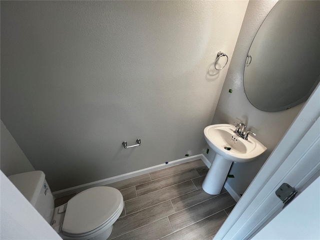 bathroom featuring wood finish floors, baseboards, a sink, and toilet