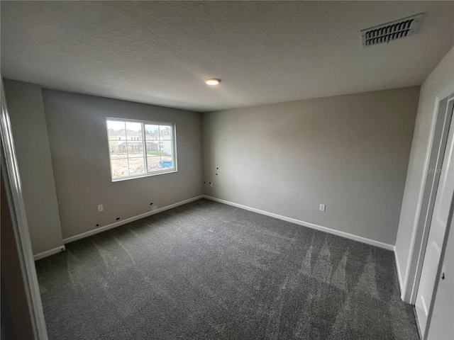 empty room with a textured ceiling, dark colored carpet, visible vents, and baseboards