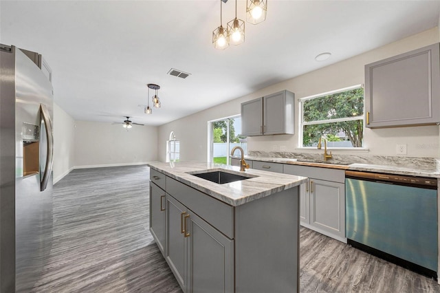 kitchen with sink, hanging light fixtures, stainless steel appliances, gray cabinets, and a center island with sink