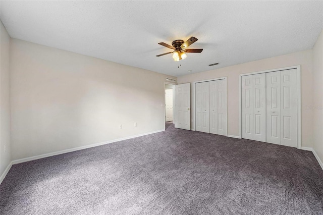 unfurnished bedroom with carpet, ceiling fan, a textured ceiling, and multiple closets