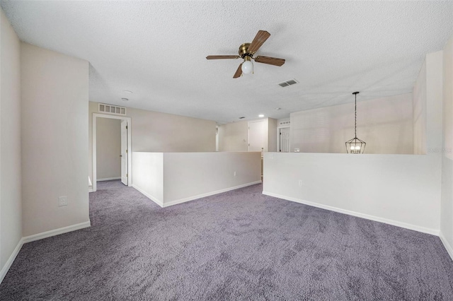 carpeted spare room featuring ceiling fan with notable chandelier and a textured ceiling