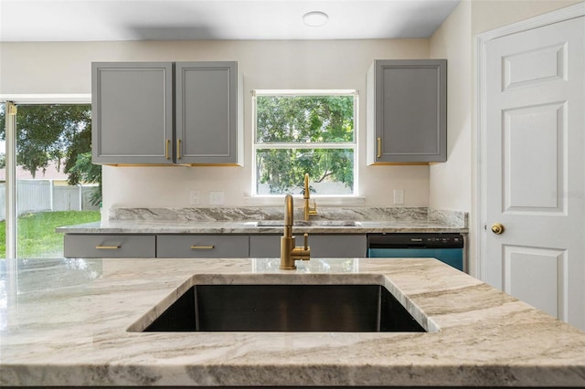 kitchen featuring light stone countertops, black dishwasher, gray cabinetry, and sink