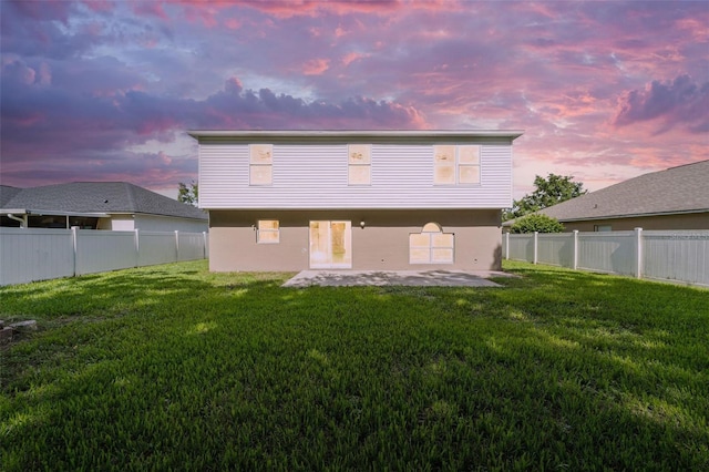 back house at dusk with a patio area and a lawn