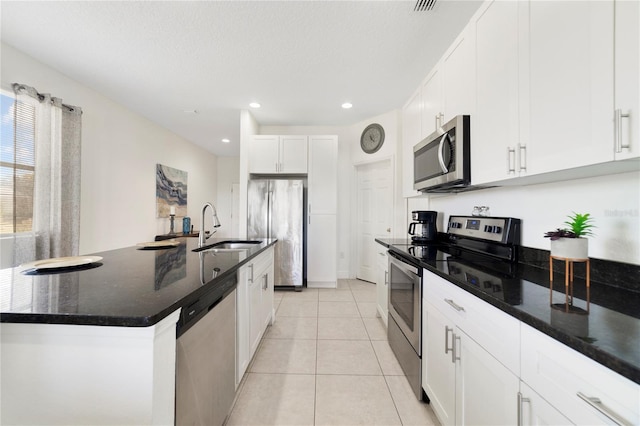 kitchen with appliances with stainless steel finishes, dark stone counters, a kitchen island with sink, sink, and white cabinetry