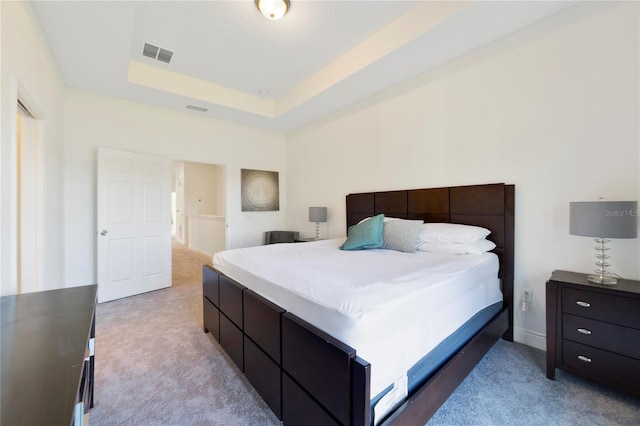 bedroom with a raised ceiling and light colored carpet