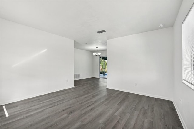 spare room featuring a chandelier and dark wood-type flooring