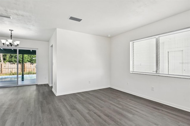 spare room with dark hardwood / wood-style flooring and an inviting chandelier