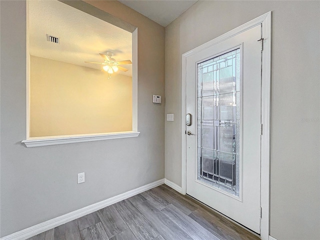 doorway featuring visible vents, baseboards, wood finished floors, a textured ceiling, and a ceiling fan