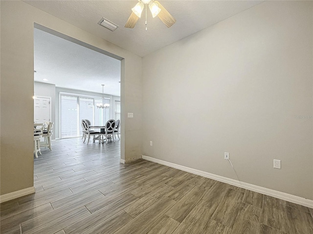 spare room featuring visible vents, baseboards, wood finished floors, and ceiling fan with notable chandelier