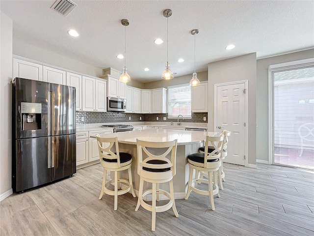 kitchen featuring a center island, hanging light fixtures, light hardwood / wood-style floors, white cabinets, and appliances with stainless steel finishes