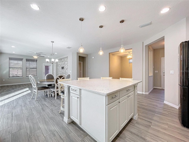 kitchen with light wood-type flooring, ceiling fan, decorative light fixtures, white cabinetry, and a kitchen island