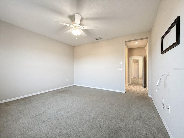 carpeted spare room with visible vents, baseboards, and a ceiling fan