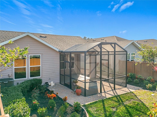 rear view of house featuring a patio, fence, roof with shingles, and a lanai