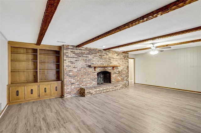 unfurnished living room with a brick fireplace, a textured ceiling, ceiling fan, beam ceiling, and light hardwood / wood-style flooring