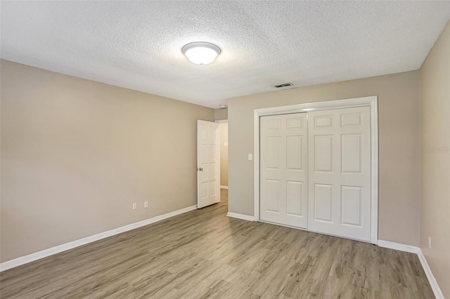 unfurnished bedroom with a closet, a textured ceiling, and light hardwood / wood-style flooring