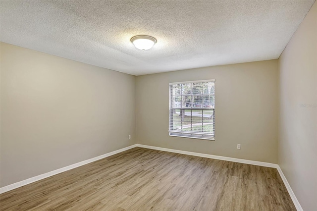 empty room with light wood-type flooring and a textured ceiling