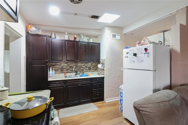 kitchen with white refrigerator, sink, light hardwood / wood-style flooring, decorative backsplash, and dark brown cabinetry