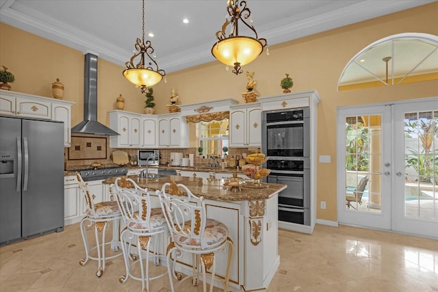 kitchen with appliances with stainless steel finishes, french doors, wall chimney range hood, white cabinets, and a kitchen island