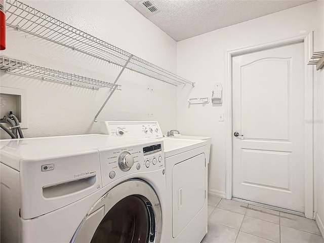 washroom with washer and clothes dryer, light tile patterned floors, and a textured ceiling