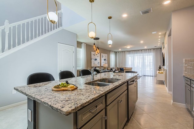 kitchen with pendant lighting, dishwasher, a kitchen island with sink, sink, and light stone counters