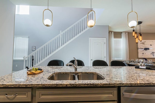 kitchen featuring light stone countertops, decorative light fixtures, dishwasher, and sink