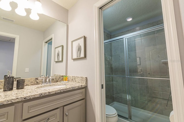 bathroom with a textured ceiling, vanity, toilet, and walk in shower