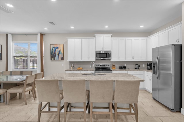 kitchen with white cabinets, sink, an island with sink, appliances with stainless steel finishes, and light stone counters