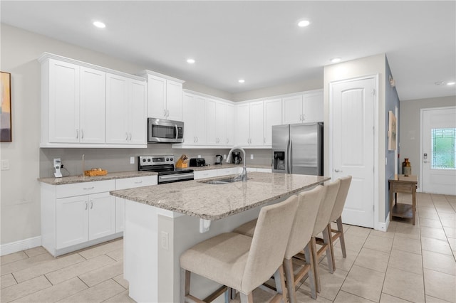 kitchen with stainless steel appliances, white cabinetry, a kitchen island with sink, and sink