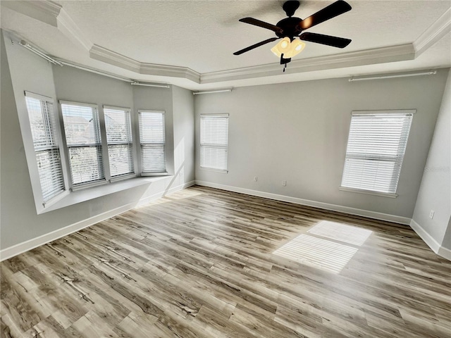 empty room with ceiling fan, light wood-type flooring, a textured ceiling, ornamental molding, and a tray ceiling