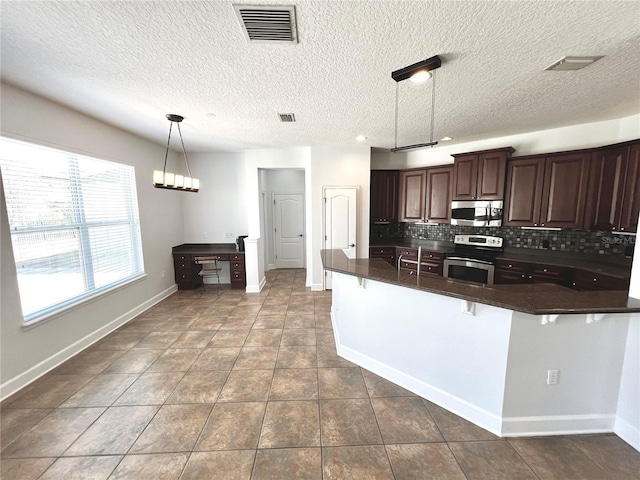 kitchen with tasteful backsplash, a textured ceiling, stainless steel appliances, hanging light fixtures, and a breakfast bar area