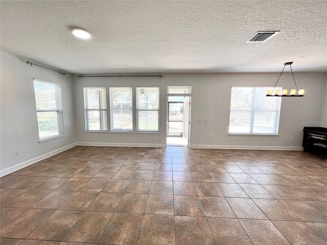 unfurnished living room with a notable chandelier, a healthy amount of sunlight, and a textured ceiling