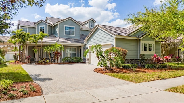 view of front of house with a tile roof, a front yard, a garage, stone siding, and driveway