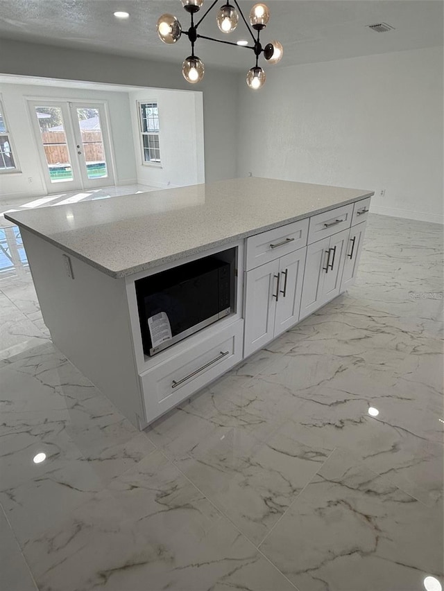 kitchen featuring white cabinetry, french doors, a center island, light stone counters, and pendant lighting