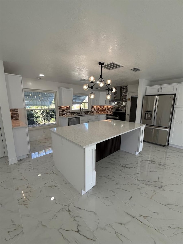 kitchen with appliances with stainless steel finishes, tasteful backsplash, decorative light fixtures, a kitchen island, and white cabinetry