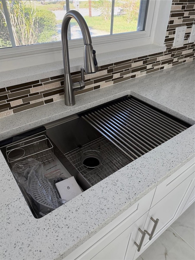 details featuring white cabinets, light stone countertops, sink, and tasteful backsplash