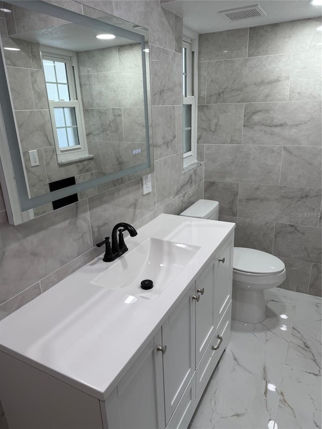 bathroom featuring vanity, tile walls, and toilet