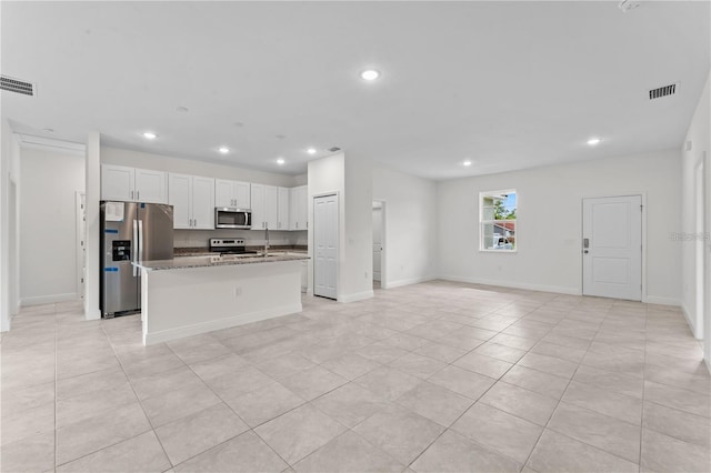 kitchen with stainless steel appliances, light tile patterned floors, dark stone countertops, an island with sink, and white cabinets