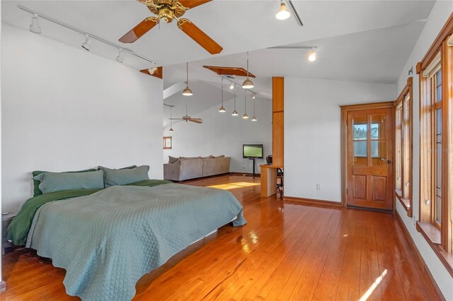 bedroom with ceiling fan, rail lighting, vaulted ceiling, and hardwood / wood-style flooring