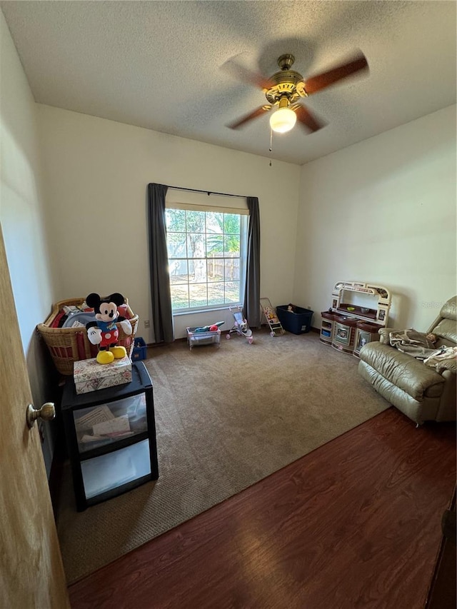 recreation room featuring wood finished floors, carpet flooring, a ceiling fan, and a textured ceiling