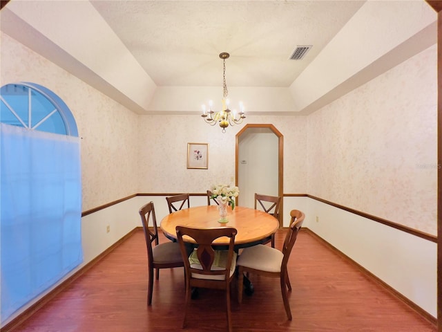 dining room with wallpapered walls, an inviting chandelier, wood finished floors, and a raised ceiling