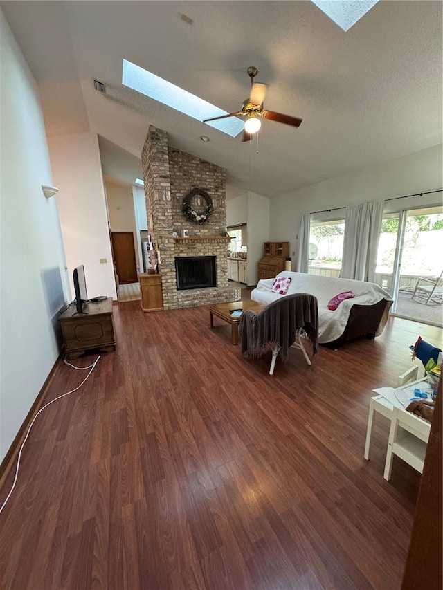 living area featuring a ceiling fan, dark wood-style floors, visible vents, lofted ceiling with skylight, and a brick fireplace