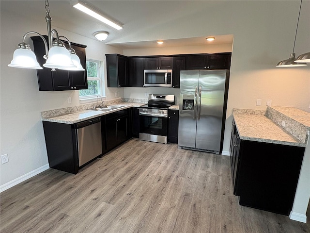 kitchen featuring light wood finished floors, dark cabinets, light countertops, stainless steel appliances, and a sink