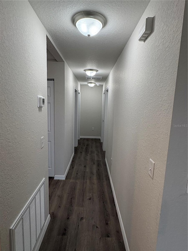 hallway featuring a textured wall, visible vents, a textured ceiling, and wood finished floors