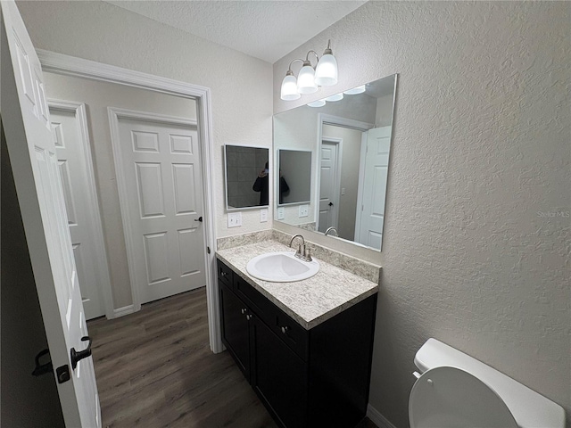 bathroom with toilet, a textured wall, wood finished floors, and vanity