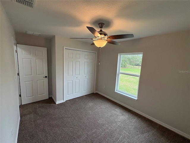 unfurnished bedroom with baseboards, visible vents, a ceiling fan, dark carpet, and a closet