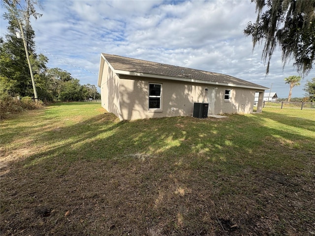 back of property with central air condition unit, fence, a lawn, and stucco siding